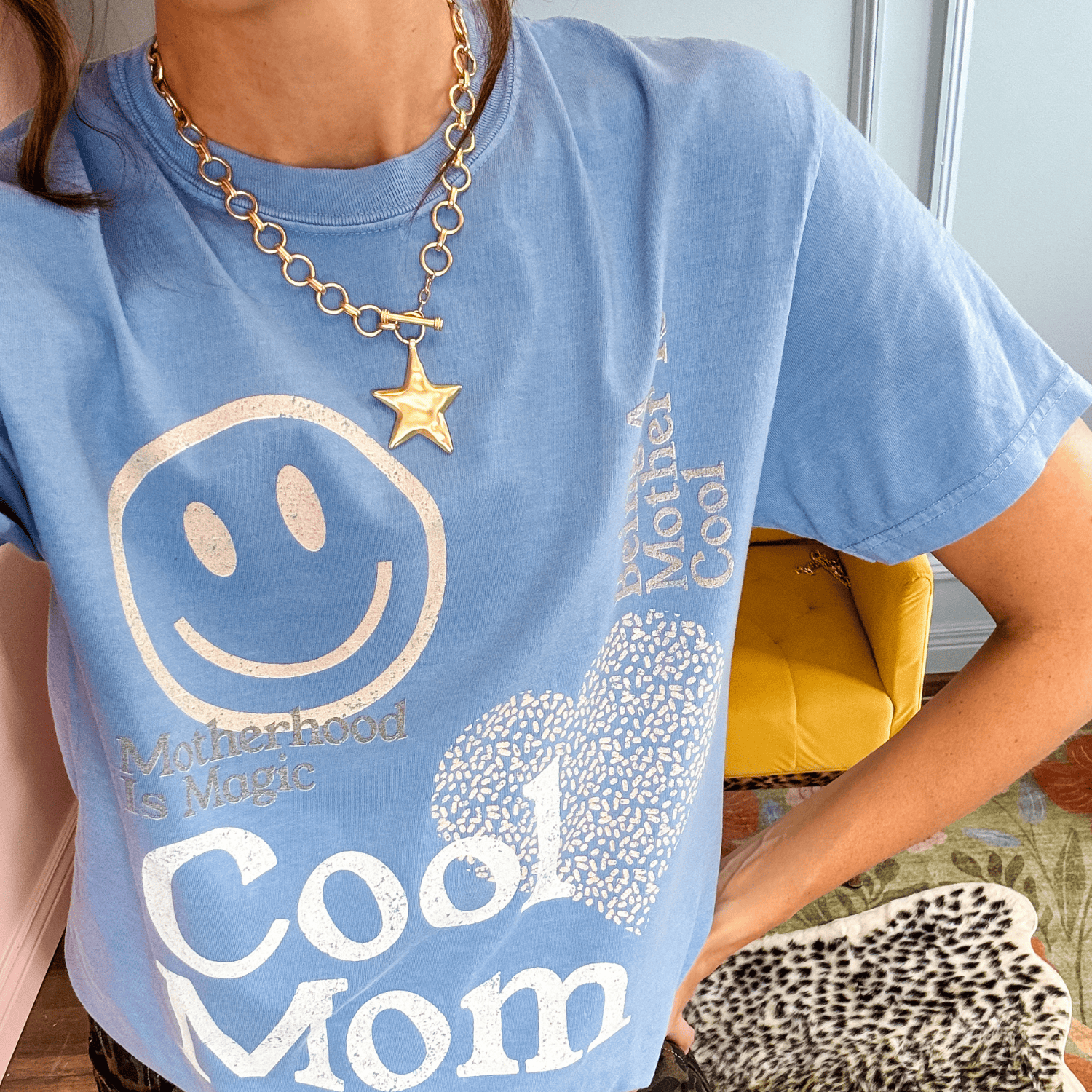 Gold star charm necklace worn over a blue graphic t-shirt with a smiley face and text.