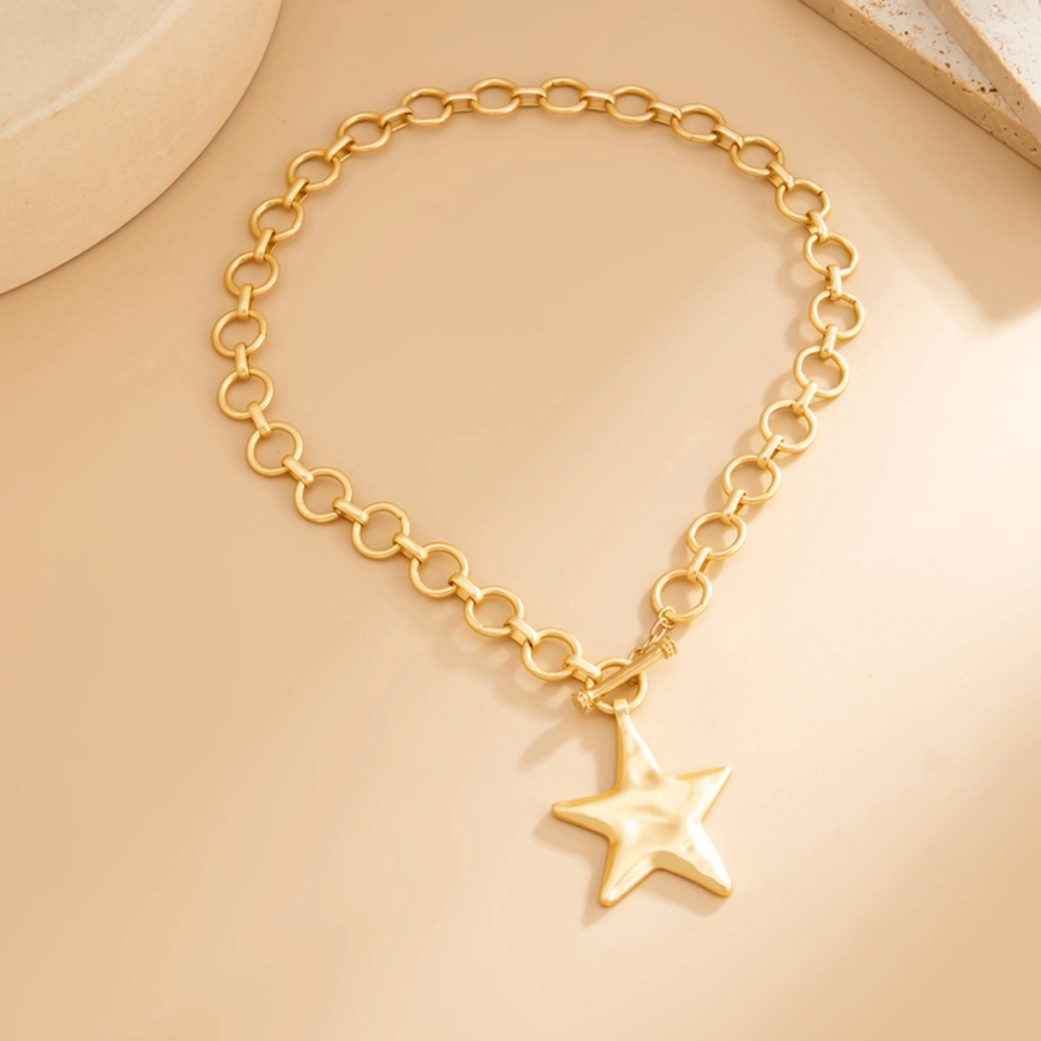 Gold star charm necklace with a chunky gold chain and a polished star pendant on a beige background.