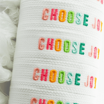 Choose Joy embroidered bracelet featuring colorful text on a white fabric band.