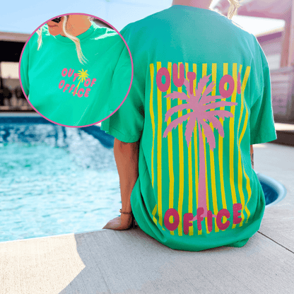 Neon Out of Office tee in teal with pink palm tree and striped design, worn by a person near a pool.
