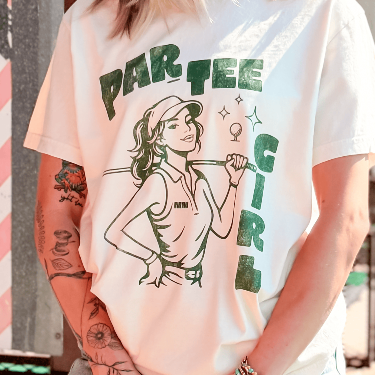 White t-shirt with a graphic design of a woman holding a golf club and text 'PAR TEE GIRL' on a blurred background.
