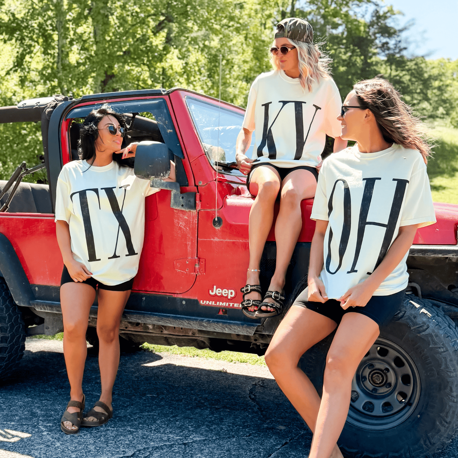 State Initial Tee in cream, featuring large black letters TX, KY, and OH, worn by three women beside a red Jeep.