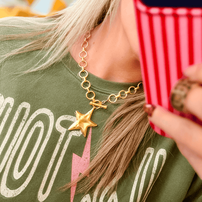 Gold star charm necklace with a chunky chain, worn by a person in a green shirt, reflecting a casual style.