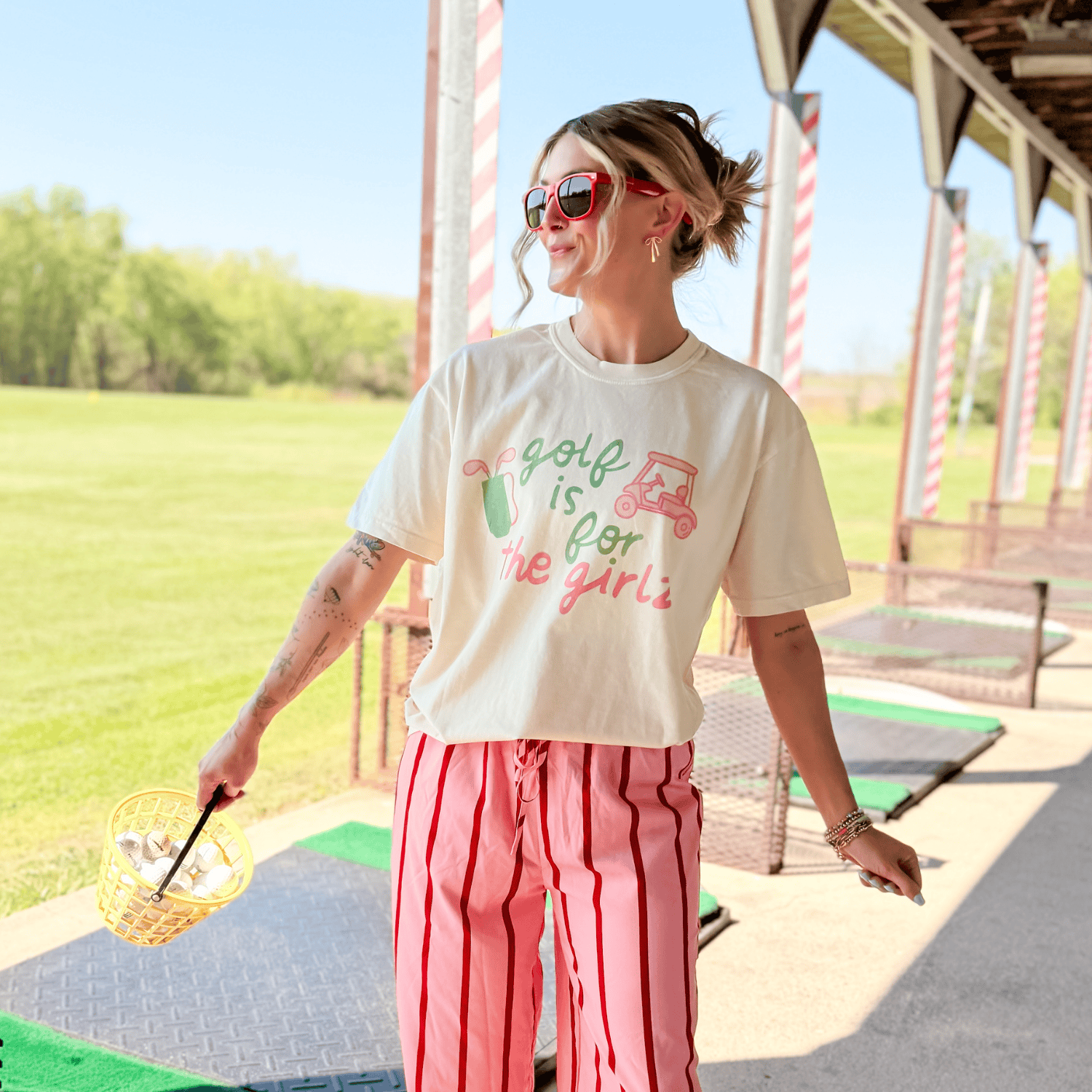 Woman wearing a t-shirt with 'Golf is for Girls' text at a golf course.